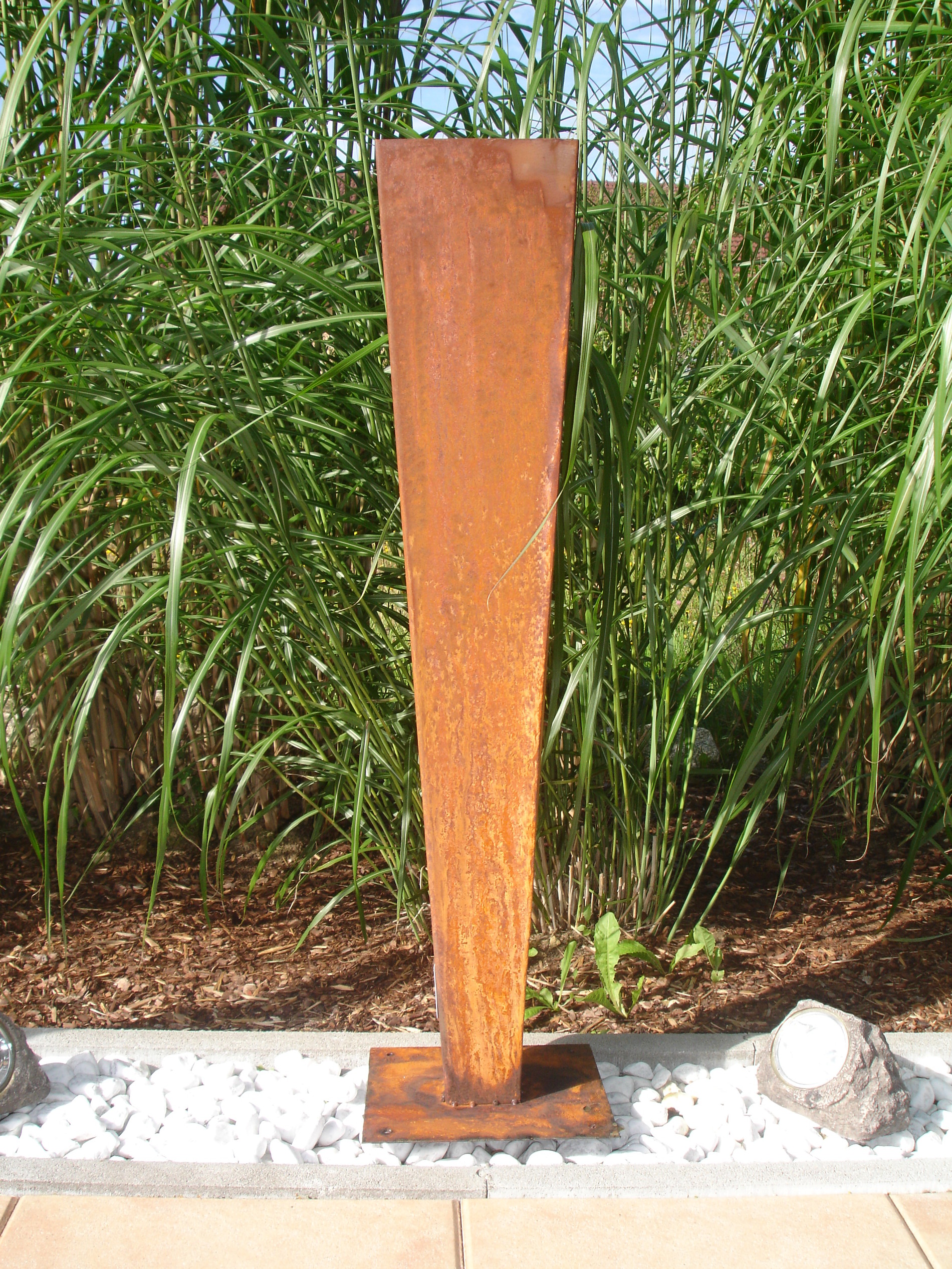 Metallsäule im Rost-Design zur Dekoration als Blickfang zwischen Ziergrassträuchern im Garten